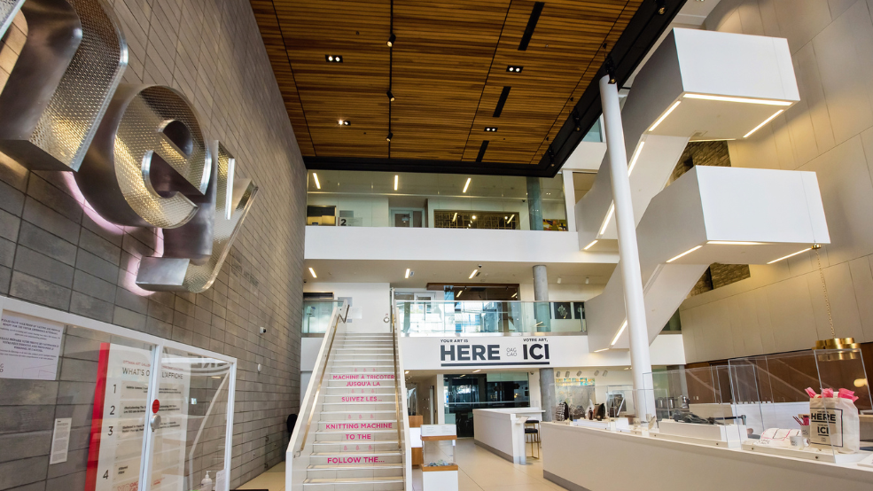 A three story atrium with wood-paneled ceiling and a large white staircase from the first to second floor.
