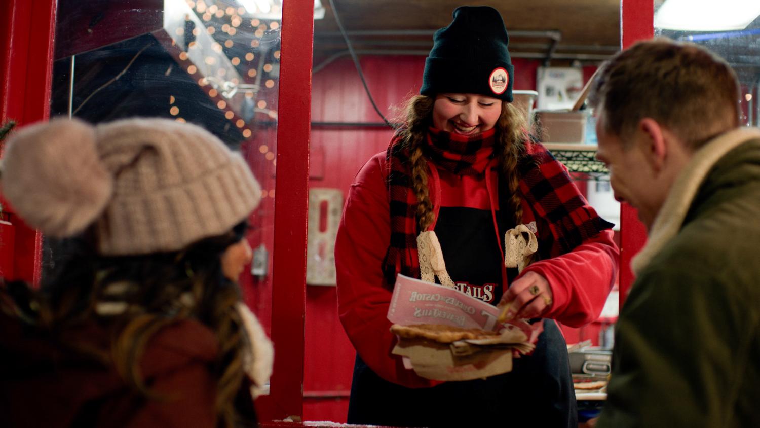 A woman serves a BeaverTail out of a food service window. 