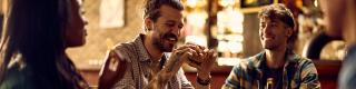 Cheerful man eating burger while gathering with friends in bar
