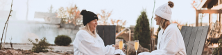 Two women in white bathrobes at an outdoor spa enjoying mimosas. 