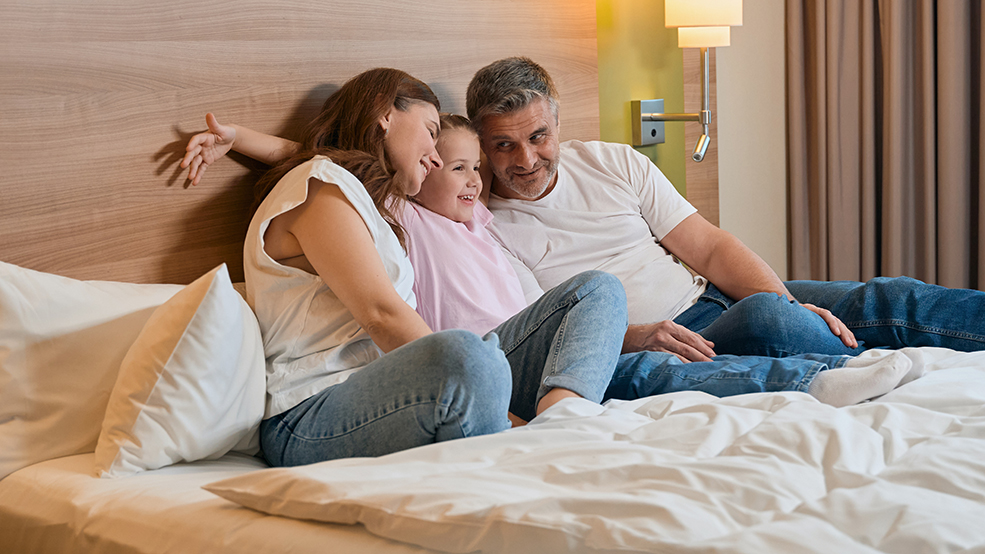 Joyful caucasian family hugging while lying on bed in hotel room